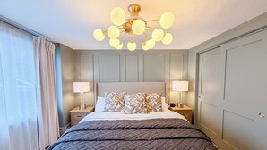 Habitación de hotel con cama, dos mesitas de noche con lámparas, lámpara en el techo y vistas al exterior a través de una ventana con cortinas.