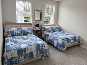 A bedroom with two beds, each with a blue and white checkered bedspread, a small bedside table with a lamp, and a mirror on the wall.