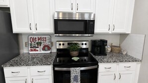 Uma cozinha com armários brancos, micro-ondas de aço inoxidável, fogão e máquina de café.