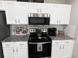 Una cocina con armarios blancos, un microondas de acero inoxidable, una estufa y una cafetera.