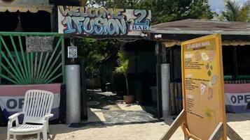 Um bar à beira-mar chamado 'Welcome to Fusion Bar', com uma placa, uma cadeira branca e uma estrutura de madeira.