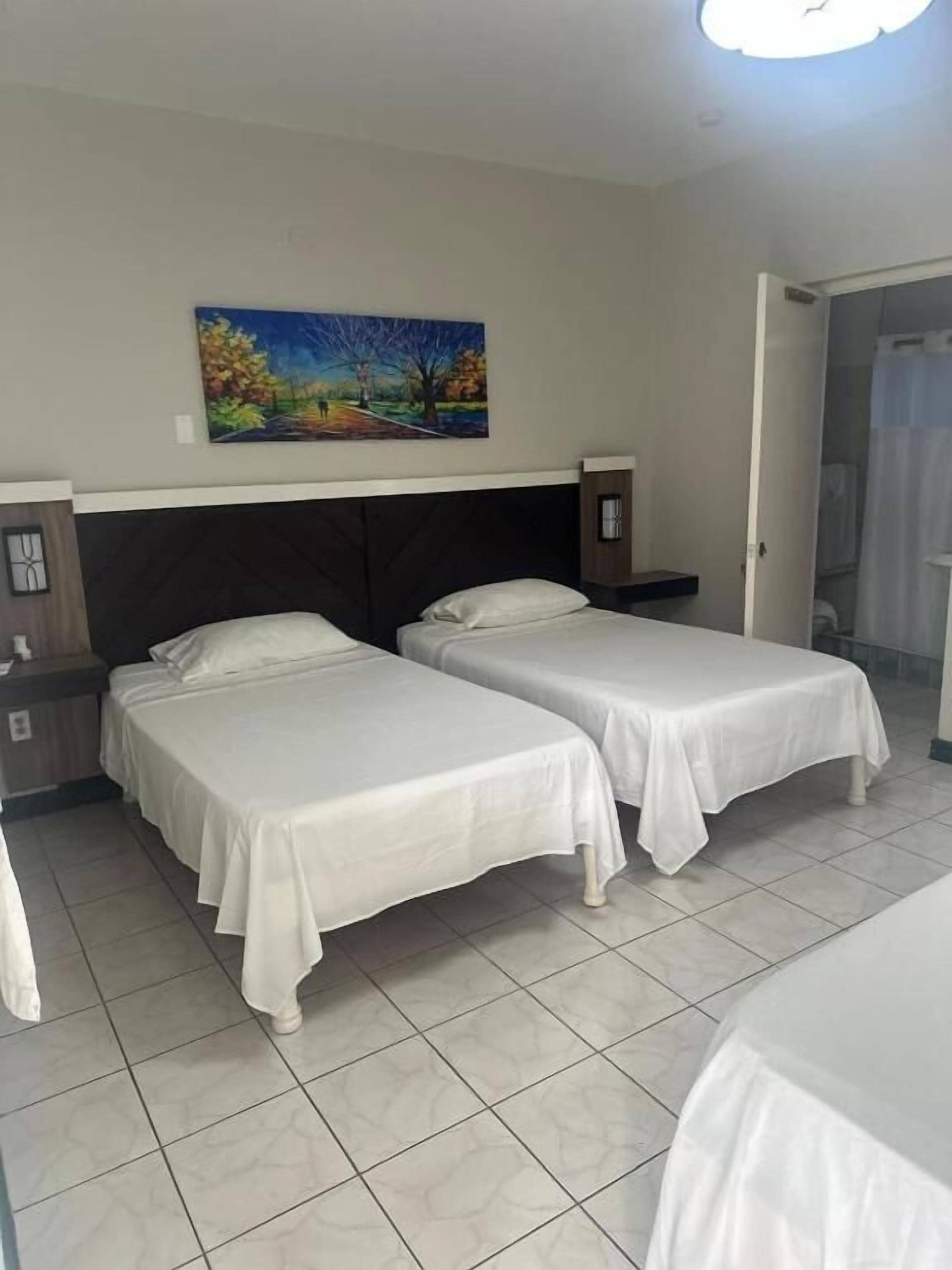 A hotel room with two beds, a painting on the wall, a nightstand, and a bathroom door.