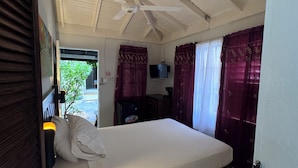 Una habitación con cama, ventilador de techo, cortinas y una pequeña mesa con un menú.