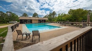 Une piscine avec des chaises longues, une terrasse en bois et un bâtiment en arrière-plan.