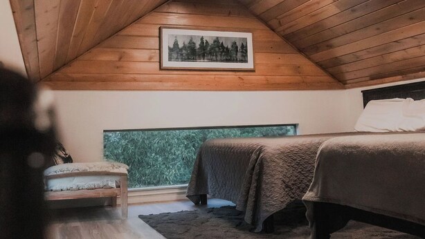 Une chambre avec un plafond en pente, un lit, une table de chevet et une fenêtre donnant sur un paysage verdoyant.