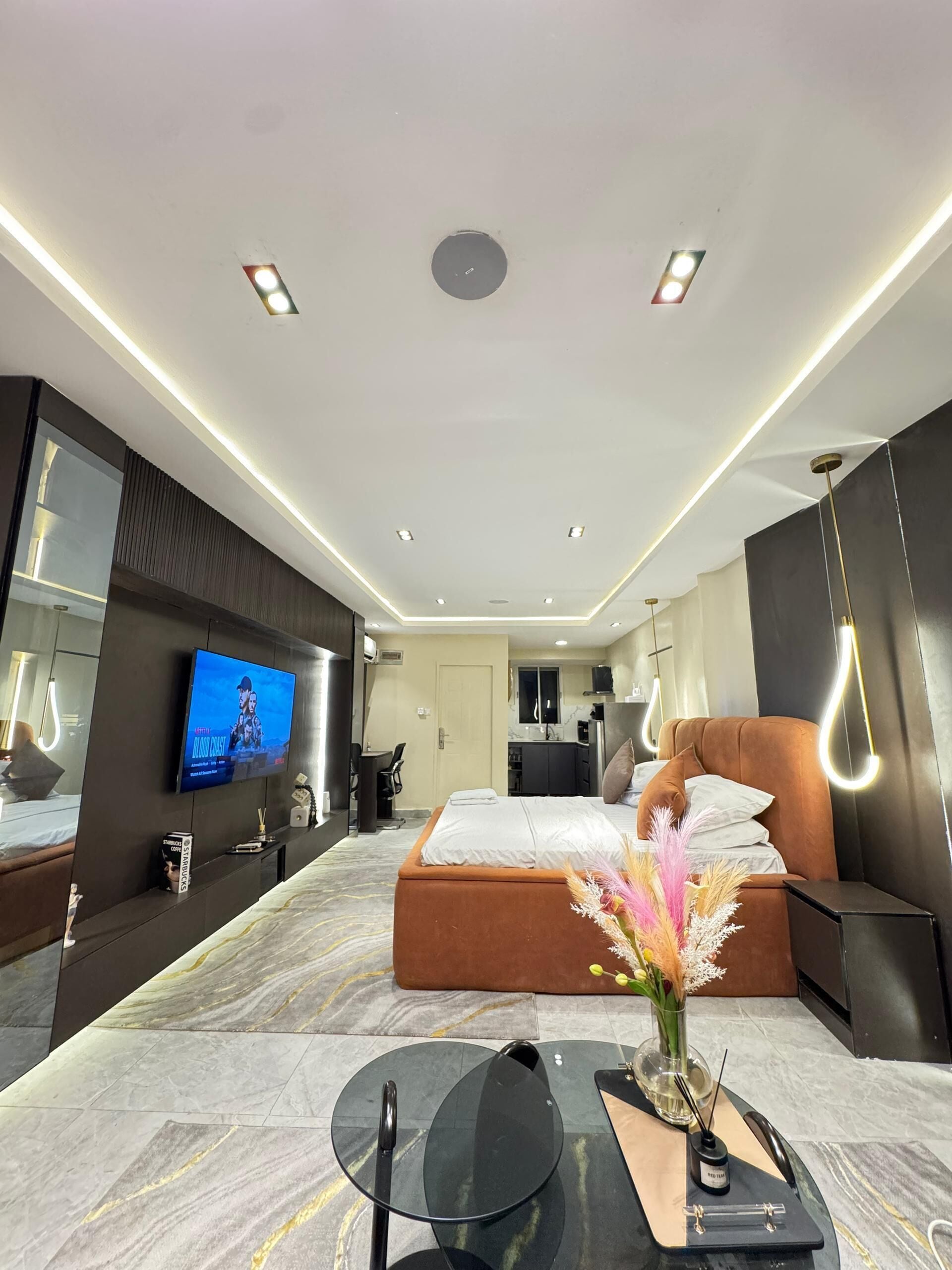 A modern hotel room with a bed, a TV, a desk, and a dining area.