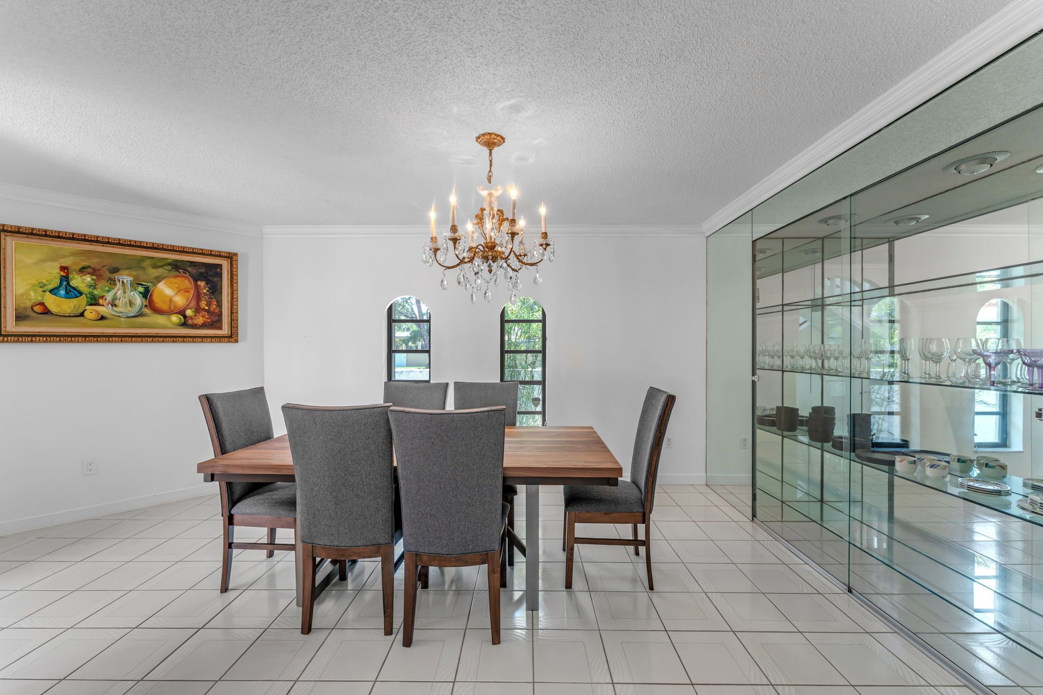 A dining room with a chandelier, a glass display case, and a painting on the wall.