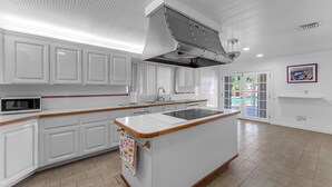 A modern kitchen with white cabinetry, a central island, a built-in microwave, and a large window. - La  Casona (Miami)