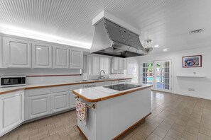 A modern kitchen with white cabinetry, a central island, a built-in microwave, and a large window. - La  Casona (Miami)