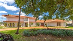 A two-story building with a tiled roof, a stone foundation, and a well-maintained lawn with various plants. - La  Casona (Miami)