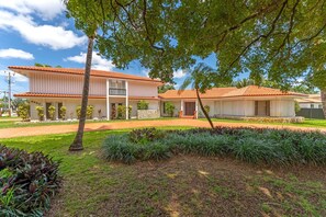 A two-story building with a tiled roof, a stone foundation, and a well-maintained lawn with various plants. - La  Casona (Miami)