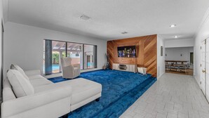 A modern living room with a white sofa, a blue carpet, and a wooden accent wall. - La  Casona (Miami)