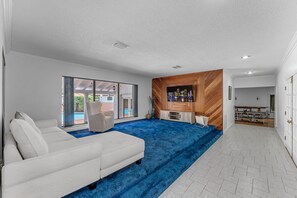 A modern living room with a white sofa, a blue carpet, and a wooden accent wall. - La  Casona (Miami)