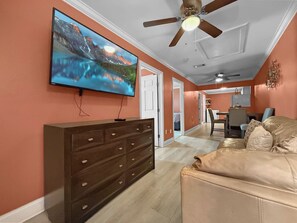 Ein Wohnzimmer mit Fernseher, Deckenventilator, Sofa und Kommode.