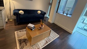 A modern living room with a dark blue sofa, a wooden coffee table, and a floor lamp. - London Bliss Apartment - Cozy Stay With City Views (London)