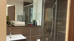 A modern bathroom with a glass shower enclosure, a white toilet, a sink, and a mirror. - London Bliss Apartment - Cozy Stay With City Views (London)