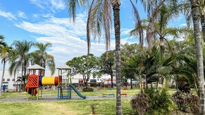 Un parque infantil con toboganes y estructuras para escalar, rodeado de palmeras y un cielo despejado.
