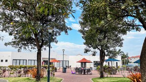 Un patio con mobiliario exterior, árboles y un edificio al fondo.