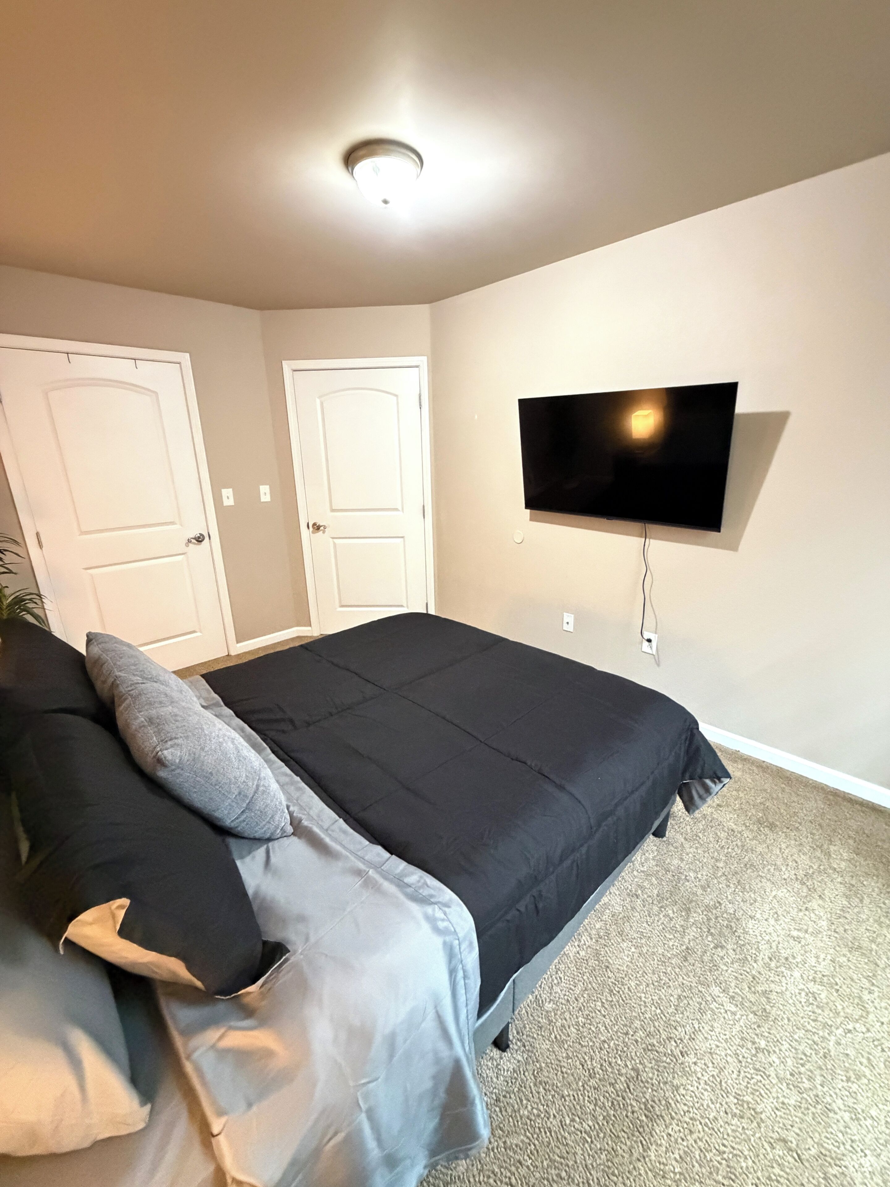 Een slaapkamer met een bed, een aan de muur bevestigde televisie en twee deuren.