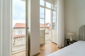 Et soveværelse med en seng, et natbord, en lampe og udsigt til en balkon med gelænder.