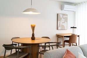 Et spiseområde med et rundt bord, stole, en vase med blomster, en pendel og en vægmonteret aircondition.