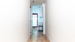 Un pasillo estrecho con piso de madera que conduce a una zona de cocina con ventana y puerta.