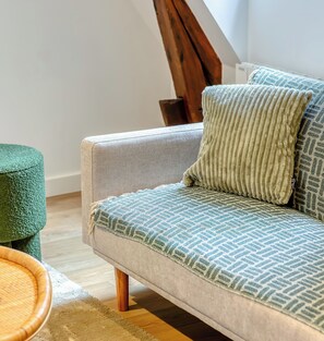 Ein Sofa mit gemustertem Bezug, ein grüner Hocker und ein Couchtisch aus Holz.
