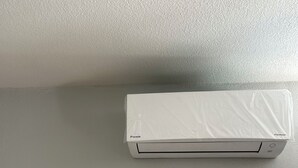 Eine weiße Klimaanlage auf einem grauen Boden, ein kleines weißes Objekt und eine grüne Metallplatte.