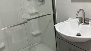 Ein Badezimmer mit einer Duschkabine aus Glas, einem weißen Waschbecken und einem Spiegel darüber.