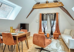 Ein Essbereich mit Holztisch und Stühlen, einem Fernseher und einem Fenster mit Vorhängen.