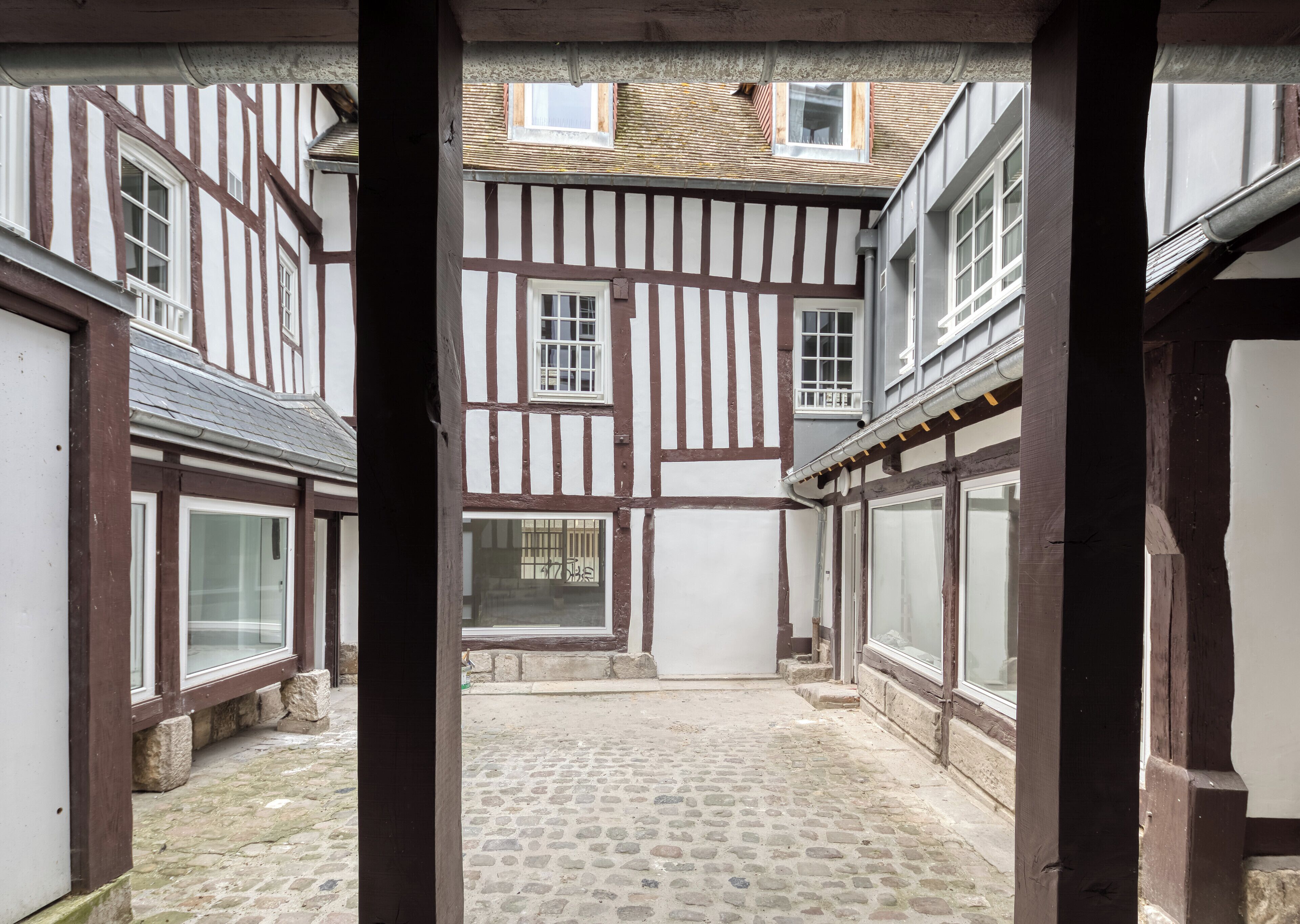 Un patio con suelo de adoquines, edificios de entramado de madera y vista a través de un arco abierto.