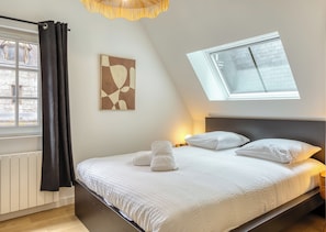 Ein Schlafzimmer mit Bett, Dachfenster, Fenster, Heizkörper und Wandbild.