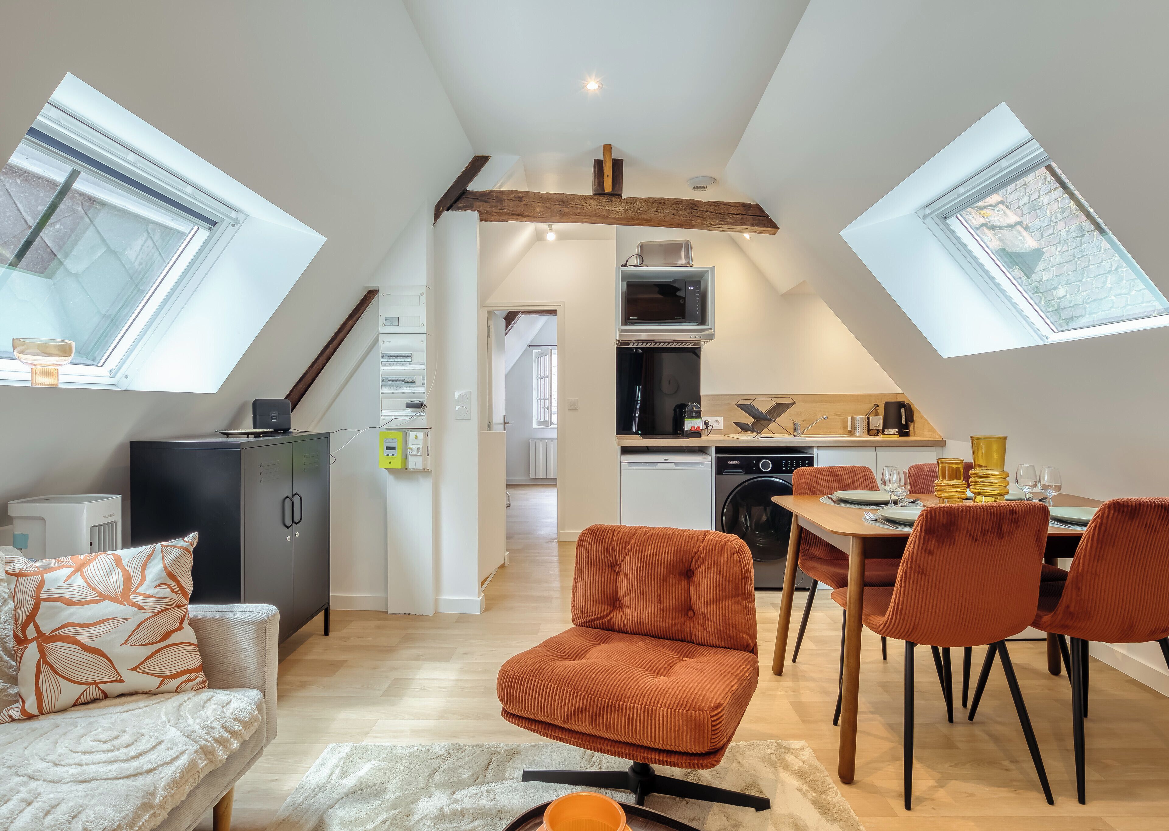 A modern loft apartment with a kitchen, dining area, and living space, featuring skylights and exposed wooden beams.