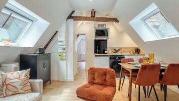 A modern loft apartment with a kitchen, dining area, and living space, featuring skylights and exposed wooden beams.