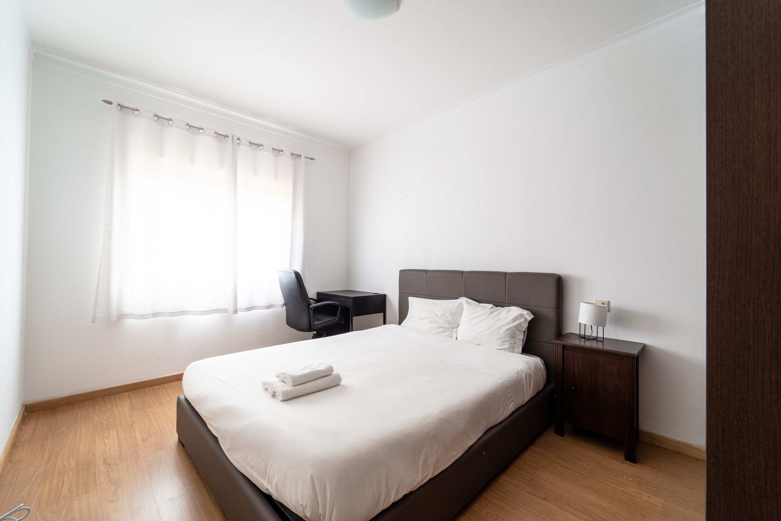 Ein Hotelzimmer mit Bett, Schreibtisch, Stuhl, Nachttisch und einem Fenster mit Vorhängen.