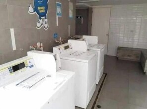 A laundry room with multiple washing machines and dryers, a wall-mounted control panel, and a door leading to another room. - Exceptional, with an ocean view, a pool, and a gym (San Miguel)