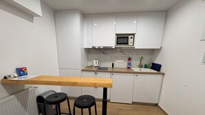 Une petite cuisine avec des meubles blancs, un plan de travail en bois, un four à micro-ondes et deux tabourets noirs.