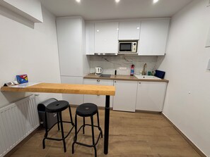 Eine kleine Küche mit weißen Schränken, einer Holzausziehtafel, einer Mikrowelle und zwei schwarzen Hocker.