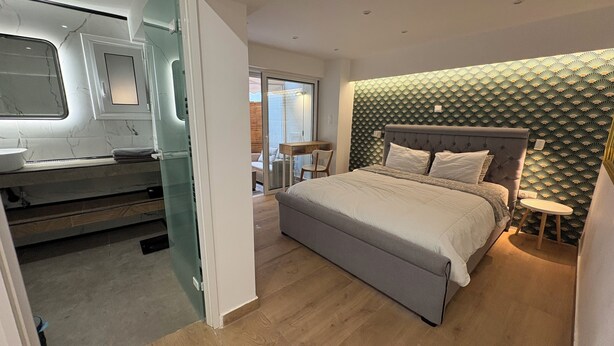 Une chambre moderne avec un grand lit, une coiffeuse avec un miroir et une porte coulissante donnant sur un balcon.