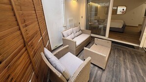 Un balcon avec des meubles en osier, une porte-fenêtre coulissante donnant sur une chambre et un mur en bois.