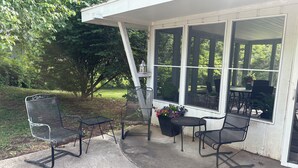 Un espace extérieur aménagé avec des chaises et une table en métal, protégé par un auvent et entouré de grandes fenêtres.