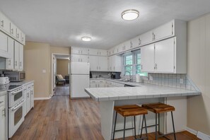 A kitchen with white cabinets, a central island with stools, a microwave, and a refrigerator. - Spacious 3 bedroom 3 Bath & bonus room house in marvelous Springfield with AC (Springfield)