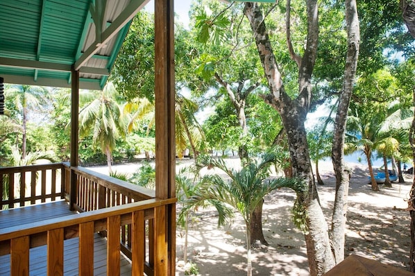 A wooden deck with a view of a sandy beach and palm trees.