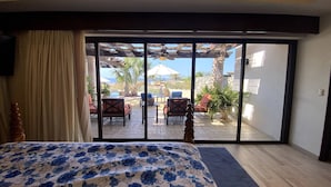 A bedroom with a bed, a view of an outdoor patio with furniture and plants, and a sliding glass door. - Oceanview Villa - The Residence at Hacienda Encantada (Cabo San Lucas)
