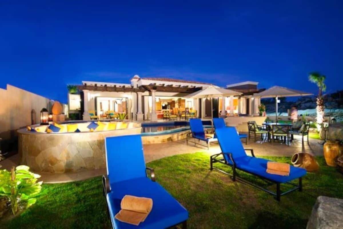 A pool area with lounge chairs, a stone structure, and a building with a patio.