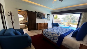A bedroom with a bed, a sofa, a dresser, and a sliding door leading to a balcony with a pool. - Oceanview Villa - The Residence at Hacienda Encantada (Cabo San Lucas)