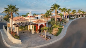 A hotel with a covered patio, palm trees, and a view of the ocean. - Oceanview Villa - The Residence at Hacienda Encantada (Cabo San Lucas)