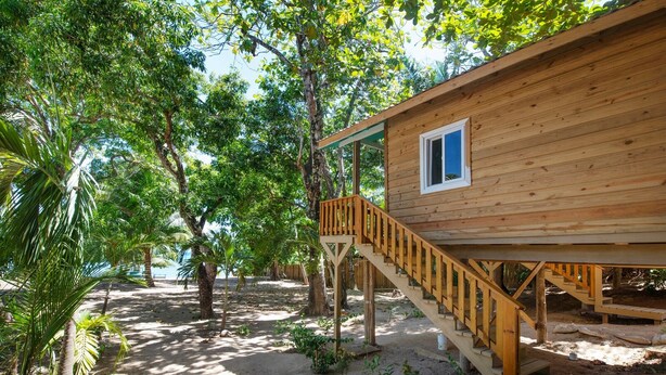 Une cabane en bois avec un escalier en bois menant à une terrasse, entourée d’arbres et de sable.