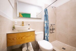Ein Badezimmer mit weißem Waschbecken, Holzwaschtisch, Toilette und Duschvorhang.