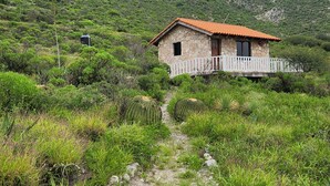 A stone house with a red roof, surrounded by greenery and a stone pathway.